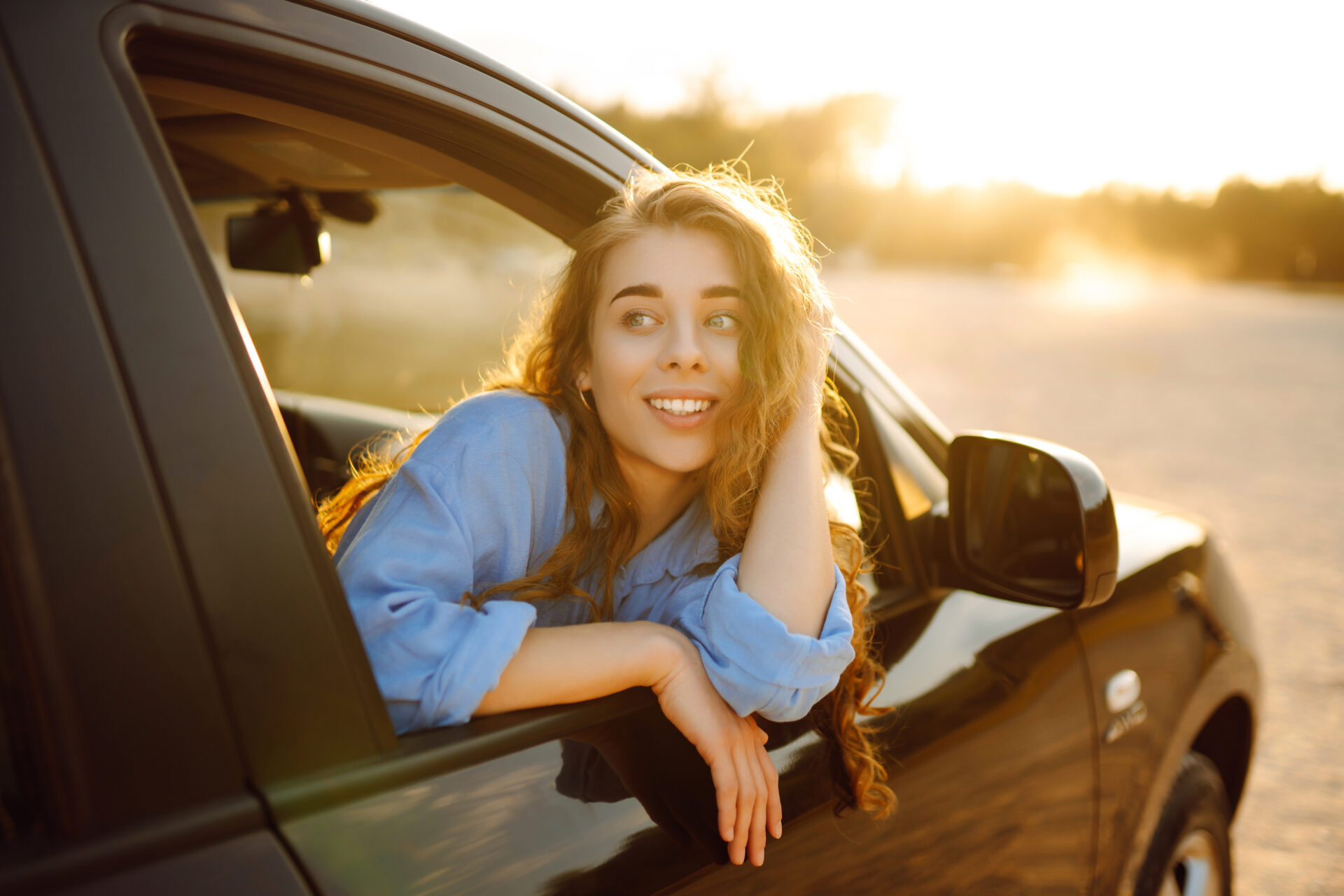 Junge, lächelnde Frau schaut aus dem Fenster eines Autos